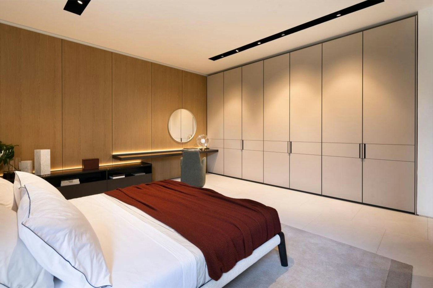A bedroom with a full height wardrobe wall and timber panelling behind the bed